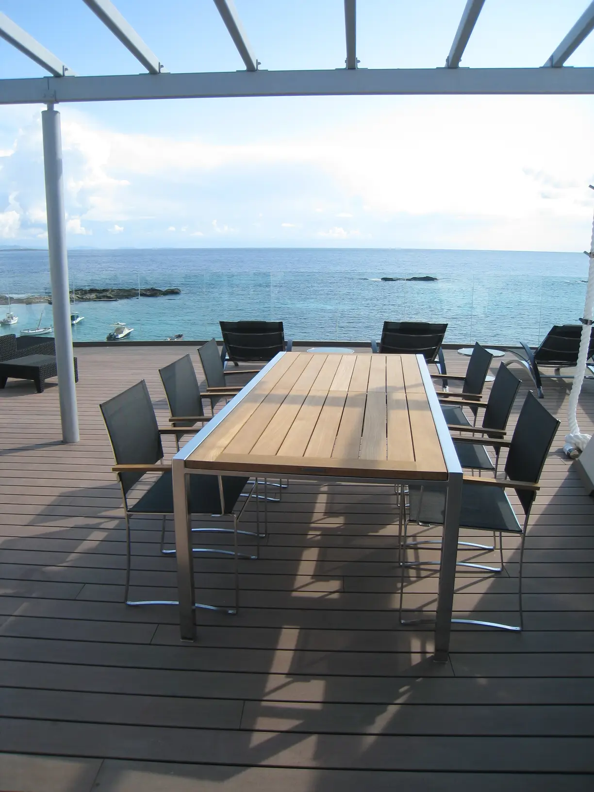 Tavolo da pranzo in teak sotto una pergola, affacciato sul mare