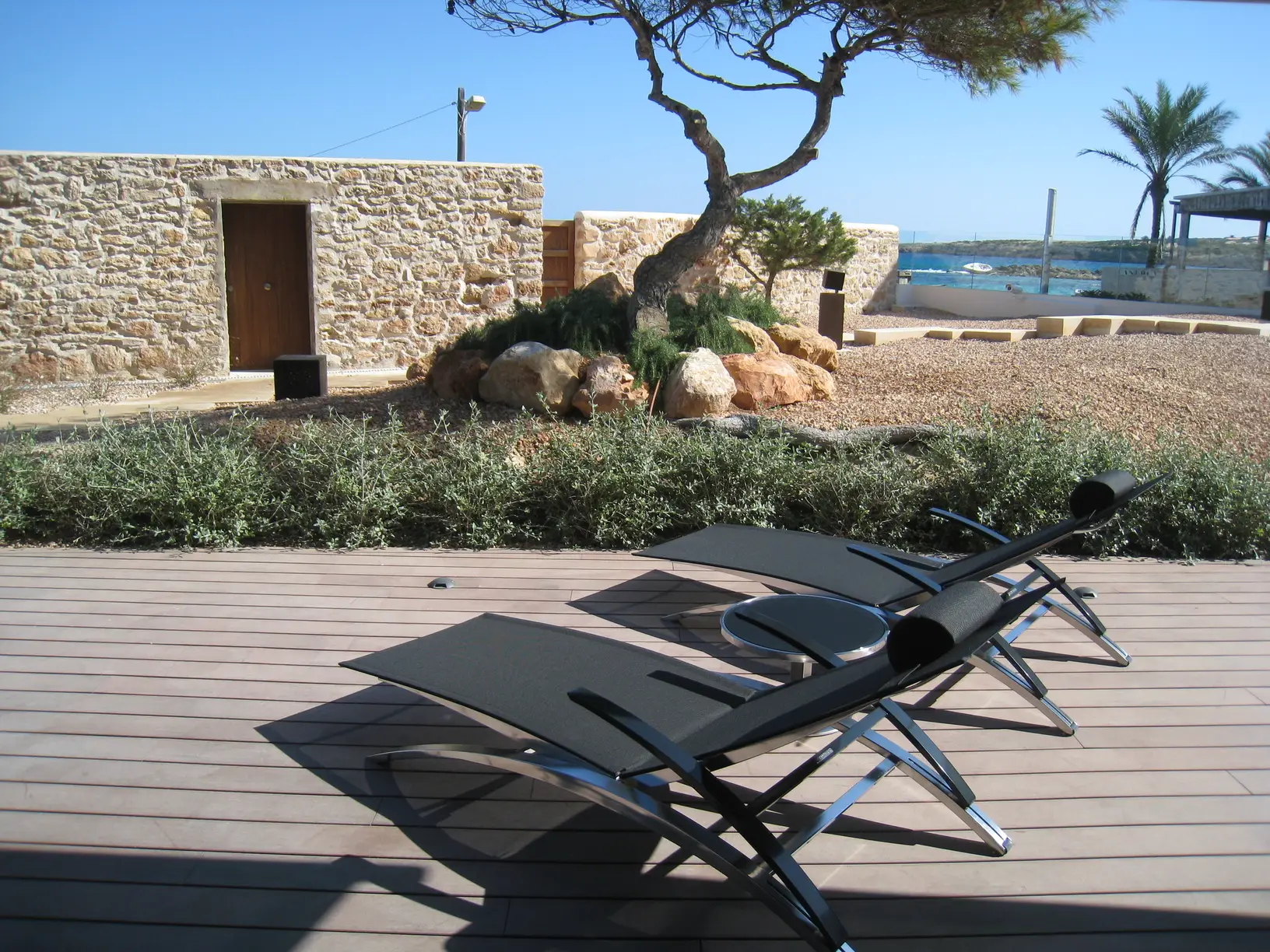Patio con muro in pietra a secco, pino marittimo e lettini su decking
