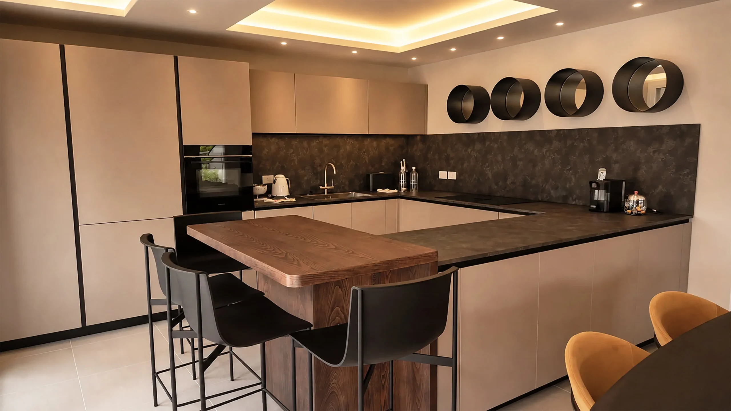 Cucina a penisola con ante laccate color sabbia, top in gres effetto pietra scura e piano snack in legno massello