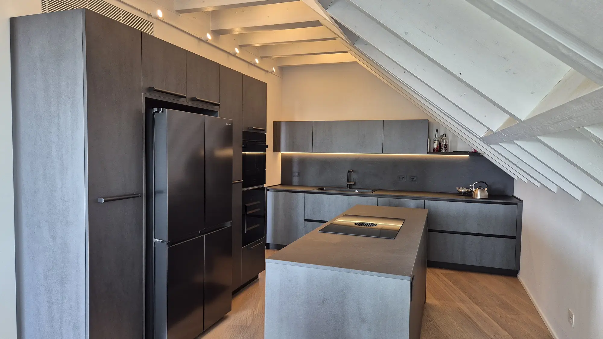 Cucina con isola in finitura effetto cemento sotto un tetto a travi bianche