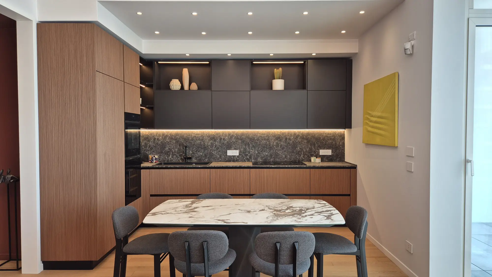 Cucina lineare in rovere e marmo scuro affacciata sul tavolo da pranzo
