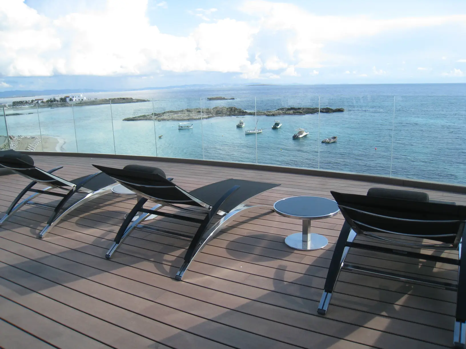 Terrazza sul mare con lettini, tavolini tondi e parapetto in vetro su decking