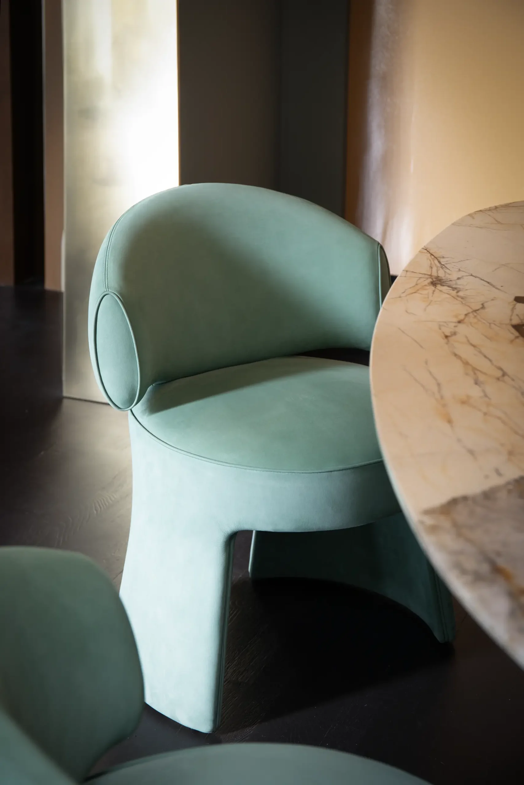 Poltroncina in velluto verde salvia accanto a un tavolo con piano in marmo