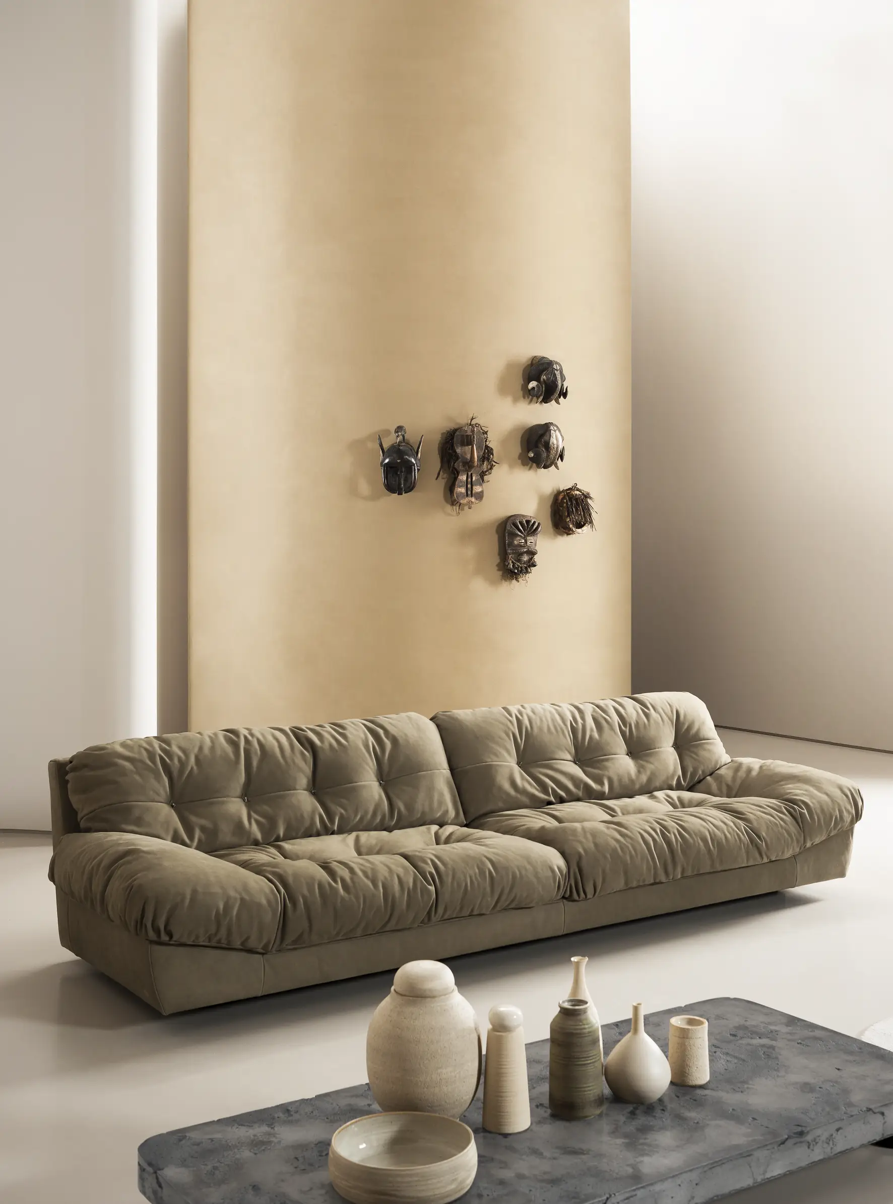 Divano capitonn&eacute; molto lungo in tessuto chiaro con ceramiche in primo piano