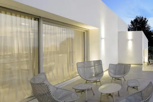 Poltroncine in rete metallica sotto un portico bianco con tende, alla luce della sera