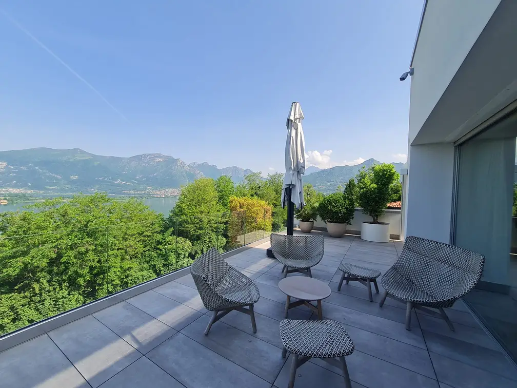 Terrazza con poltroncine in rete metallica, ombrellone e vista sulle montagne