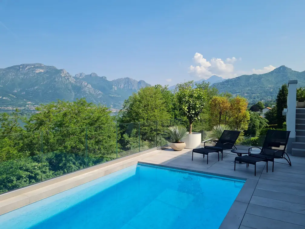 Piscina a filo pavimento con lettini e agrumi in vaso, affacciata sul lago