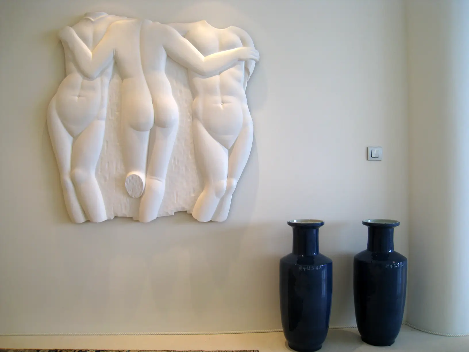 Bassorilievo figurativo in pietra chiara accanto a due vasi blu notte