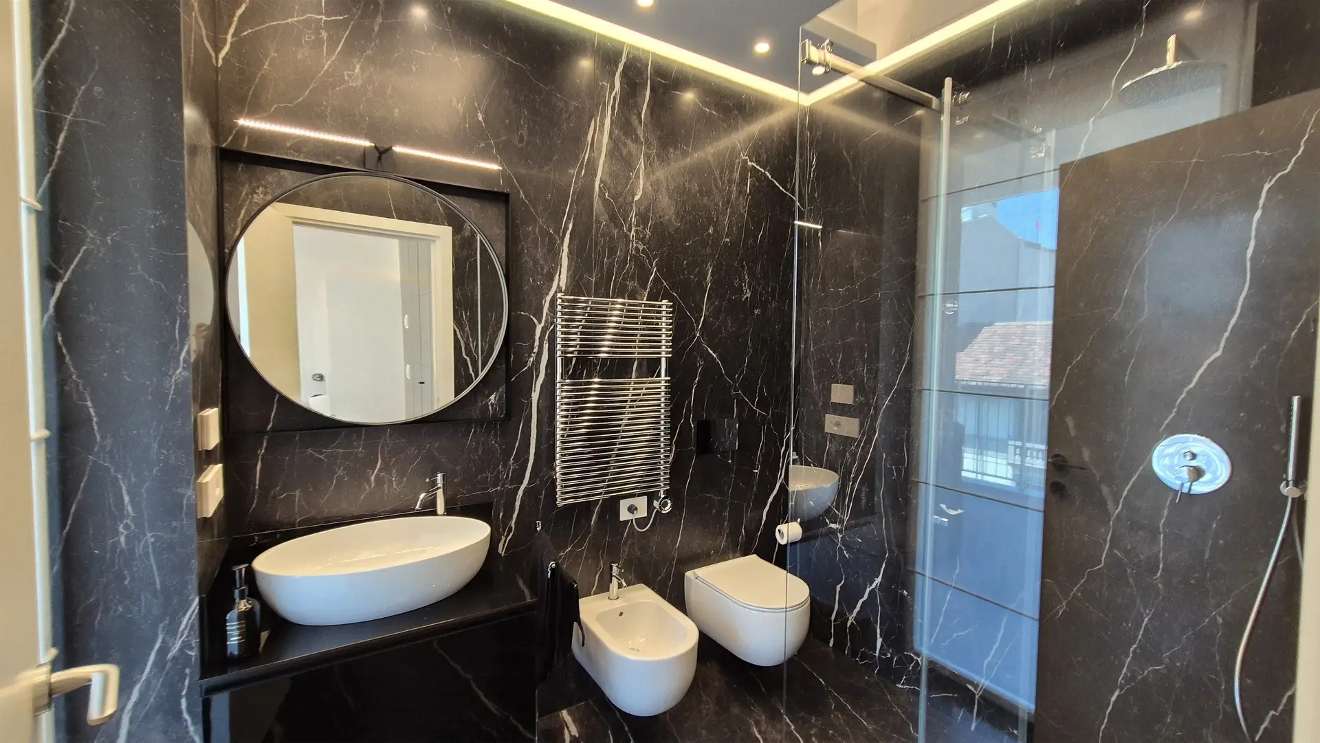 Bagno con rivestimento effetto marmo nero, lavabo d&rsquo;appoggio e sanitari bianchi